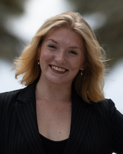 Smiling blonde woman in a pinstripe blazer standing outdoors, facing the camera.