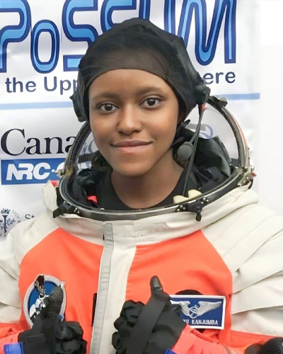 Young woman in an orange spacesuit and helmet, smiling at the camera with a space program backdrop behind her.