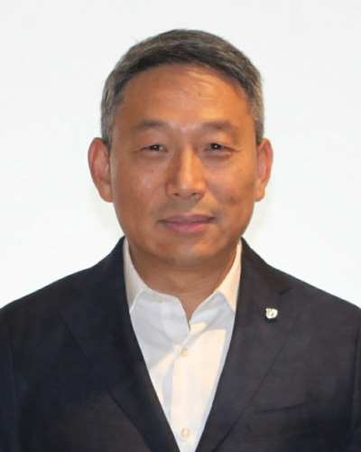 Professional headshot of a middle-aged Asian man in a dark suit and white shirt, facing the camera with a neutral background, shoulders visible.