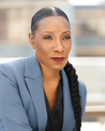 Meredith Beckford-Smart | ISDC 2026 Professional woman in a blue blazer with a long braided ponytail, looking pensively to the side.