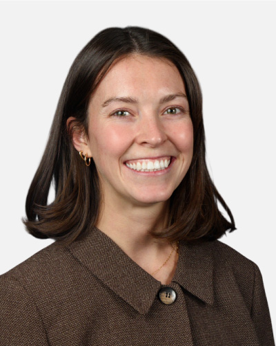 Portrait of a smiling woman with shoulder-length dark hair wearing a brown blazer, looking at the camera.