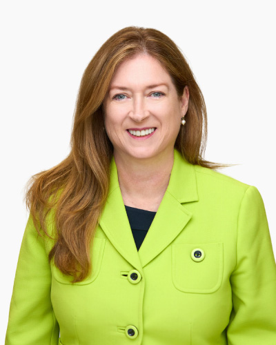 Roseanne Healy | ISDC 2026 Professional portrait of a smiling woman with long light brown hair wearing a lime green blazer against a white background.