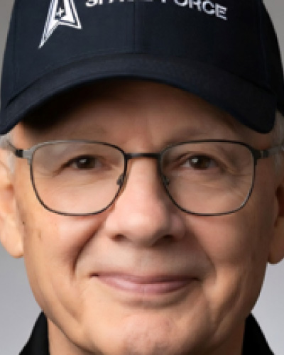 Jack-Kennedy | ISDC Close-up of a smiling man wearing glasses and a dark cap with the Space Force insignia.