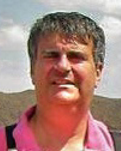 Man in a pink polo shirt outdoors, with hills and a blue sky behind him.